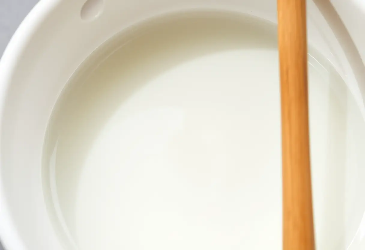 Un bol en porcelaine blanche contenant du monomère, éclatant sous la lumière naturelle, avec une baguette de mélange en bois